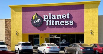 Planet Fitness gym building facade with several cars parked in front of it.